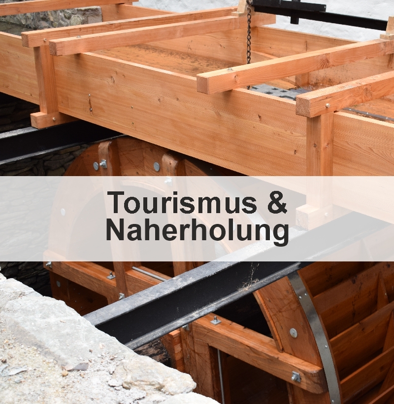 Das Bild zeigt ein historisches hölzernes Wasserrad. In der Mitte des Bildes findet sich die Aufschrift: "Tourismus & Naherholung".